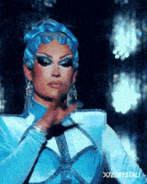 a drag queen is wearing a blue and white outfit with the name xiecrystali written on the bottom