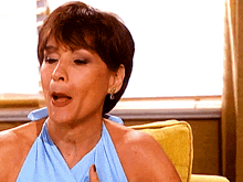 a woman in a blue dress is sitting on a yellow couch with her mouth open