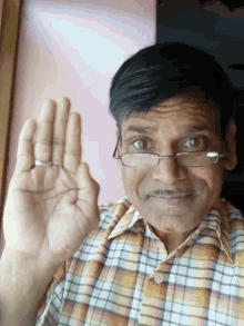 a man wearing glasses and a plaid shirt is holding his hand up
