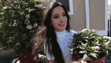 a woman is holding a potted plant in front of a house .