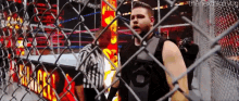 a wrestler is standing behind a chain link fence .