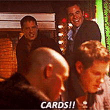 a group of men are sitting around a table and one of them says " cards "