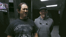 a man in a metallica shirt says " you 're such a boring guy " while standing next to another man