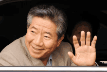 a man in a suit is smiling and waving his hand