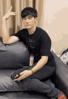 a man sitting on a couch wearing a black shirt that says ' tk '