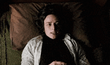 a man in a black shirt is laying on a bed with a brown pillow and a green blanket
