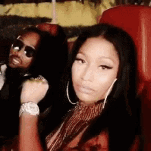 a woman is sitting in a red chair next to a man wearing sunglasses and a watch .