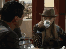 a woman in a cowboy hat is drinking from a cup while a man looks on