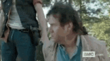 a man is sitting on the ground with his arm up in the air while another man stands behind him .