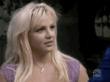 a woman with blonde hair is wearing a purple shirt and necklace .