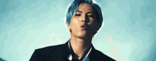 a young man with blue hair is wearing a suit and making a face .