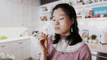 a woman is smelling something in a kitchen with a sign that says delish on it