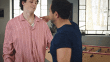 a man in a pink striped shirt touches another man 's neck