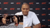 a man in a white shirt is sitting in front of a ufc wall .