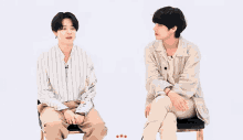 two young men are sitting next to each other on chairs and talking to each other .