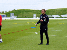 a man in a nike jacket stands on a soccer field talking to another man