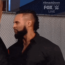 a man with a beard is standing in front of a chain link fence with fox live written on the bottom