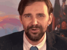 a man with a beard in a suit and tie looks at the camera