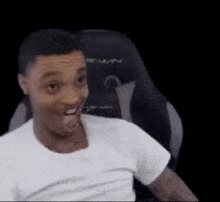 a man in a white shirt is sitting in a chair and making a surprised face .