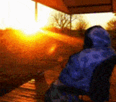 a person in a blue hoodie is looking out a window at the sun