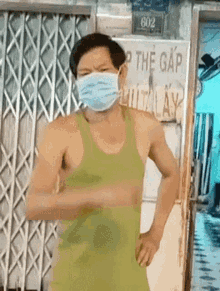 a man wearing a mask and a green tank top is standing in front of a gate .