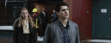 a man in a leather jacket is standing in front of a group of people and says who are you .