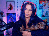 a woman wearing headphones holds a small dog in front of a shure microphone