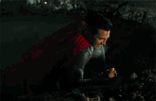 a man in a superman costume is laying on the ground with a torch in his hand .