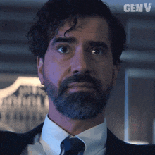 a man with a beard wearing a suit and tie with the word genv on the bottom right