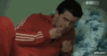 a man in a red jacket is laying on a bed holding a cigarette .