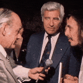 a man in a suit is holding a microphone and talking to another man
