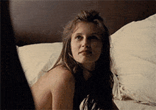 a woman without a shirt is laying on a bed with white sheets