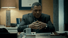 a man in a suit sits at a desk with a name plate that says j. crawford