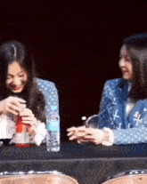 two women are sitting at a table with a bottle of water and a bottle of soda .