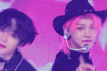 a man with pink hair and a cowboy hat is standing next to another man with pink hair and a microphone .