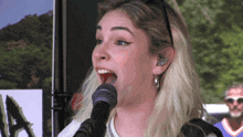 a woman singing into a microphone with the letter a on the wall in the background