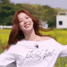 a woman is standing in a field with her arms outstretched and wearing a white shirt that says pocket girl .