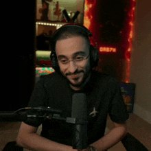 a man wearing headphones and glasses is giving a thumbs up while sitting in front of a microphone .