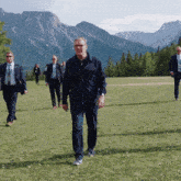 a group of men are walking in a grassy field with mountains in the background