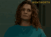 a woman with red curly hair is wearing a blue sweater with the word wentworth on the bottom