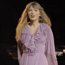 a woman in a purple dress is standing on a stage in front of a crowd .