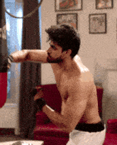 a shirtless man is hitting a punching bag with his fist in a living room