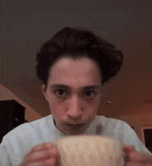 a young man is drinking from a white cup .