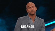 a bald man in a suit points at the word bhaskar