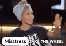 a woman with a towel wrapped around her head and a t-shirt that says `` mistress take the wheel '' .