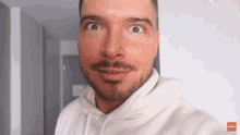 a man with a beard is wearing a white hoodie with a red button that says " subscribe "