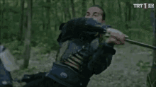 a man in armor is holding a sword in front of another man with a trt 1 hd logo on the bottom right