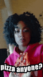 a woman in a pink hoodie is holding a slice of pizza with the caption pizza anyone ?