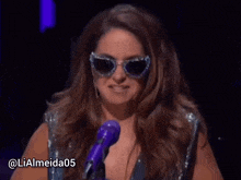 a woman wearing sunglasses stands in front of a purple microphone with the hashtag lialmeida05