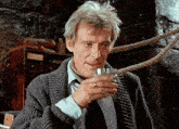 a man in a gray sweater is drinking from a glass